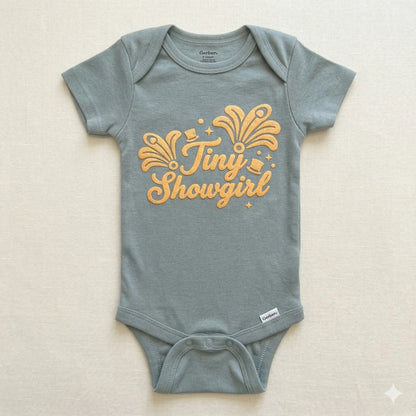 Gray baby onesie with 'Tiny Showgirl' text on a beige background