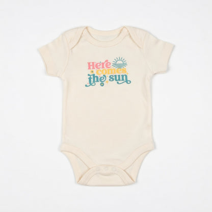 Beige baby onesie with 'Here comes the sun' text on a white background