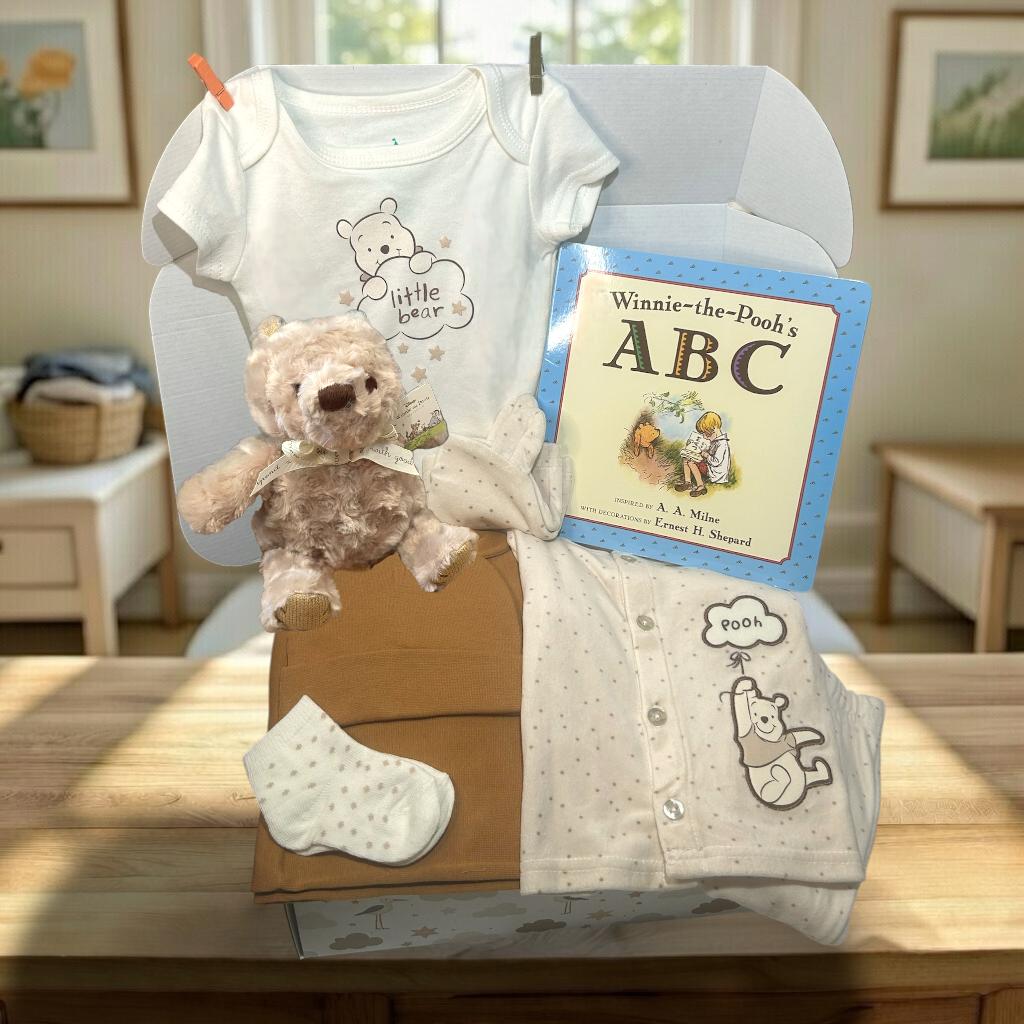 Baby gift set with onesie, teddy bear, book, and sock on a table.