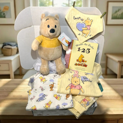 Collection of Winnie the Pooh-themed baby items including a plush toy, blanket, and book on a chair.