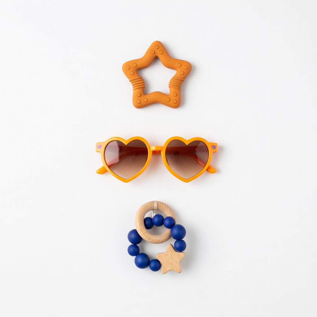 Orange star-shaped teether, orange heart-shaped sunglasses with brown lenses, and a blue beaded ring with a wooden star on a white background.